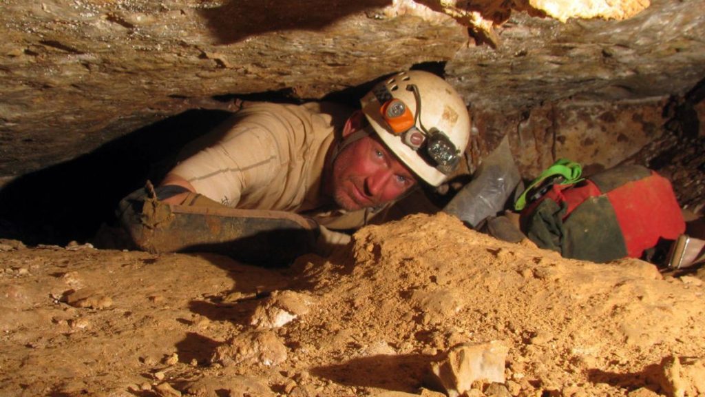 A man squeezes through a tight passage in a cave.