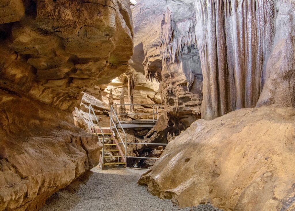An image shows a walkway leading to a staircase inside Crystal Onyx Cave in Kentucky.